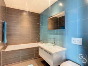 Une salle de bain carrelée bleue avec toilettes et lavabo.