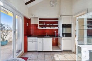 Une cuisine avec des murs carrelés rouges et une porte vitrée.