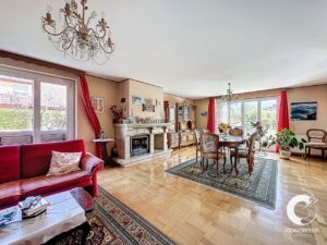 Salon élégant avec coin repas, doté d'une cheminée, d'un lustre et de fenêtres drapées rouges, décorées avec goût avec des meubles et des plantes.
