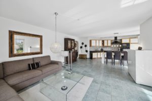 Intérieur de salon spacieux avec cuisine ouverte, mobilier moderne et carrelage au sol.
