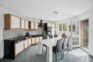 Intérieur de cuisine moderne avec des murs blancs, des armoires en bois, un comptoir noir et un coin repas menant à une porte patio.