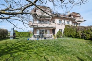 Une maison spacieuse avec un patio et un grand jardin par une journée ensoleillée.
