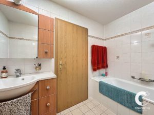 Une petite salle de bains bien éclairée avec des murs carrelés blancs, un meuble en bois et des serviettes colorées.