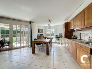 Cuisine lumineuse et spacieuse avec armoires en bois et coin repas doté de grandes fenêtres et de carrelage.
