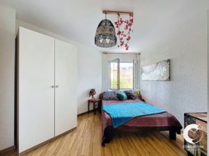 Chambre lumineuse avec un lit simple, une armoire et une suspension au motif floral.