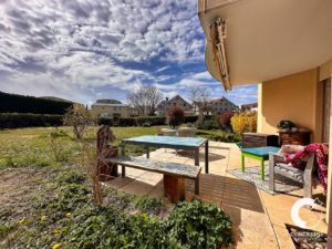 Cour arrière ensoleillée avec un coin salon patio et une pelouse bien entretenue, sous un ciel bleu vif avec des nuages épars.