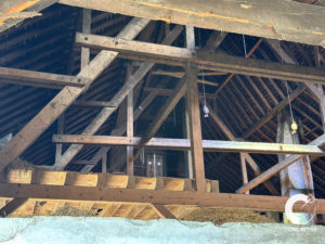 Vue intérieure de la structure du toit en bois d'une ancienne grange avec poutres et chevrons apparents.