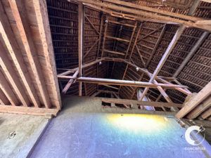 Intérieur d'un grenier en bois avec chevrons apparents et rayon de soleil au sol.
