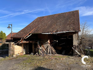 Une vieille grange endommagée avec un mur extérieur partiellement effondré sous un ciel clair.