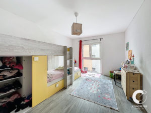 Une chambre d'enfant bien organisée avec un lit superposé, une armoire, un bureau et une fenêtre laissant entrer la lumière du jour.