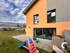 Maison orange moderne avec de grandes fenêtres, une cour arrière et un toboggan pour enfants.