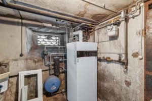 Une chaufferie au sous-sol dotée d'un système de chauffage moderne avec des tuyaux et des compteurs contre des murs en béton vieillis.