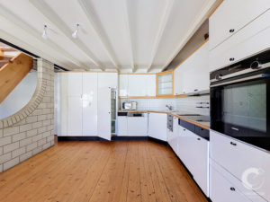 Modern kitchen with white cabinets, built-in Siemens ovens, wooden countertops, and a curved brick wall on the left.