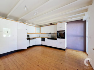 Modern L-shaped kitchen with white cabinets, wooden countertops, and built-in oven under a purple wall.