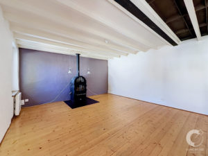 Interior room with white exposed ceiling beams and a black wood stove against a purple accent wall.