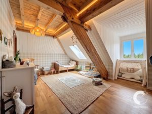 Cozy children's attic playroom with exposed wooden beams, a skylight, and a soft beige rug on a wooden floor under a sloped ceiling.