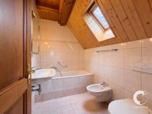 Bathroom with white tiles, wooden sloped ceiling, skylight, bathtub, sink, bidet and toilet.