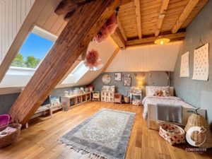 Cozy children's attic bedroom with sloped wooden beams, skylights, and toy storage along the wall.