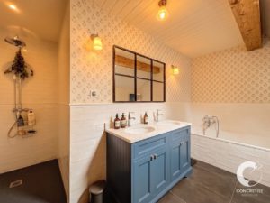 Blue double-sink vanity with marble countertop in a patterned bathroom, large grid mirror, and a white tiled tub area to the right.