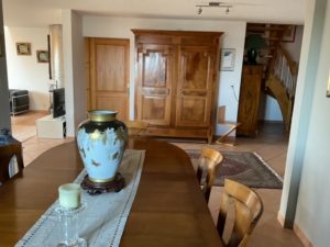 Wood dining table with a blue and gold vase centerpiece, candle, and a wooden armoire in a bright living area.