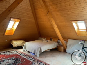 Cozy attic bedroom with a sloped wooden ceiling, bed, and a bicycle resting by the wall near a skylight window.