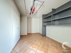 Laundry/storage room with a ceiling-mounted drying rack and clothes hanging, white cabinets on the left, gray metal shelves on the right, beige tiled floor