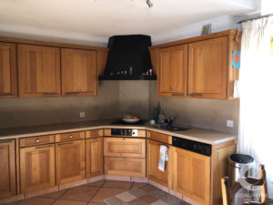 L-shaped kitchen with wooden cabinets, beige counters, and a black range hood over the stove; sink and dishwasher along the right wall.