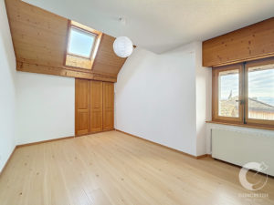Bright empty attic room with sloped wooden ceiling, skylight, and built-in wooden wardrobe doors.