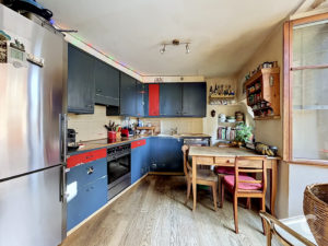 Modern kitchen with dark blue cabinets, stainless steel refrigerator, and a wooden dining table by a window.