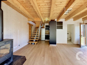 Open-plan living space with exposed wooden beams, stairs, and a modern kitchen area along the back wall.