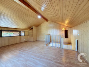 Spacious room with light wood paneling on walls and ceiling, wooden floor, and a metal railing around a stairwell area.