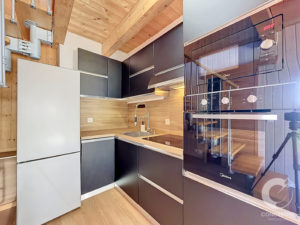 Modern kitchen with black cabinets, wooden ceiling beams, and built-in stainless appliances including an oven and fridge