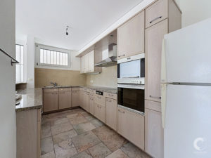Modern L-shaped kitchen with light wood cabinetry, built-in double oven, and stainless range hood.