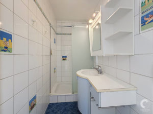 Bright tiled bathroom with a walk-in shower, white vanity, and mirror.