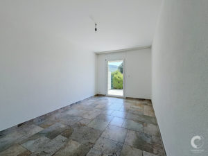 Empty white room with tiled floor, a single hanging light bulb, and a door with a window showing outdoors.