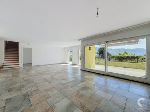 Bright, empty living space with large glass doors to the yard and hills, and a tiled floor; staircase on the left.