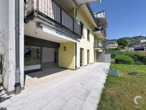 Apartment building with yellow exterior, multiple balconies, and a tiled patio under a clear blue sky.