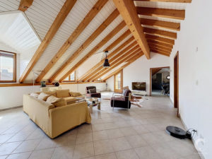 Open living room with exposed wooden ceiling beams, large windows, beige sofa, and glass coffee table.