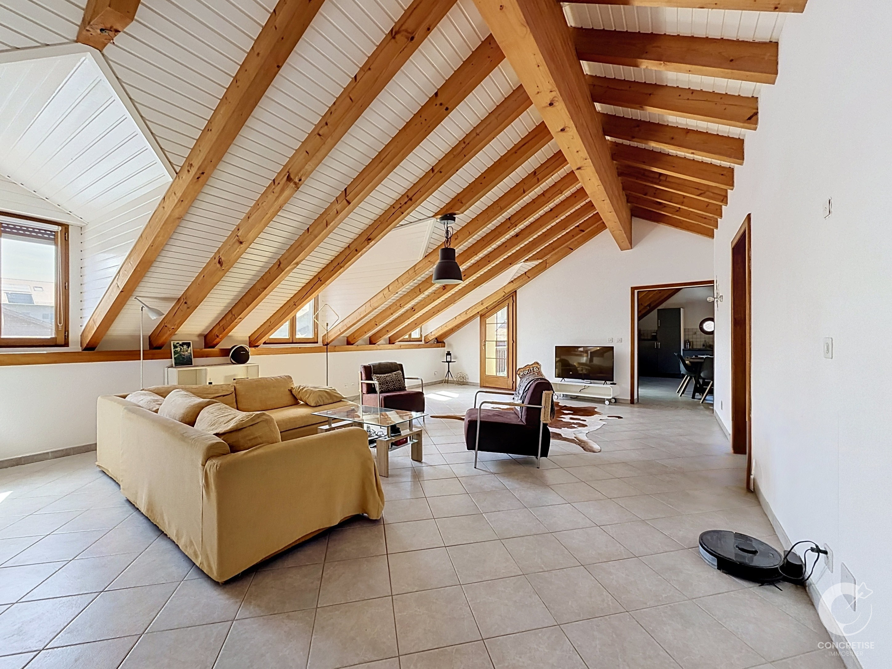 Open living room with exposed wooden ceiling beams, large windows, beige sofa, and glass coffee table.