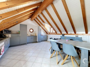 Attic-style kitchen with exposed wooden beams, white panel ceiling, gray cabinets, and a dining table with blue chairs.