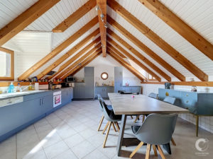 Kitchen with exposed wooden beams and a vaulted ceiling, gray lower cabinets, and a long dining table.