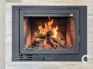 Wood-burning fireplace insert with glowing embers and stacked logs, set in a stone surround.