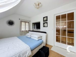 Bright white bedroom with a low bed, blue sheets, white quilt, sheer curtains, wall-mounted TV, and a glass-paned door on the right.