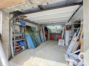 A cluttered garage workshop with shelves, glass panes, and a red tool chest at the back, ready for stored building materials and tools.
