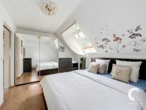 Bright bedroom with a large mirrored wardrobe, white bed, and floral wall decals under a skylight window.