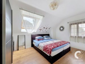 Bright bedroom with a double bed, blue bedding, and a red pattern throw under a skylight with sheer curtains.