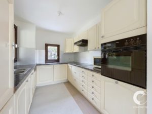 L-shaped cream kitchen with granite countertops, built-in oven and microwave, and a window above the counter.