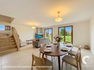 Open-plan living and dining area with a wooden staircase, gray sofa, TV, and large French doors to a green yard; a floral centerpiece on the dining table.