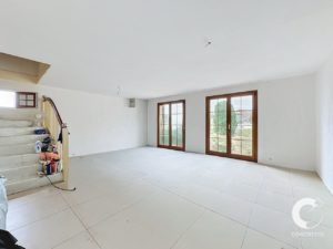 Bright unfurnished living room with white walls, large wooden-framed glass doors opening to the yard, and a staircase on the left with renovation supplies.