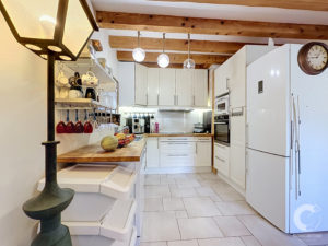 Bright modern kitchen with white cabinets, wood ceiling beams, and three hanging glass pendant lights."